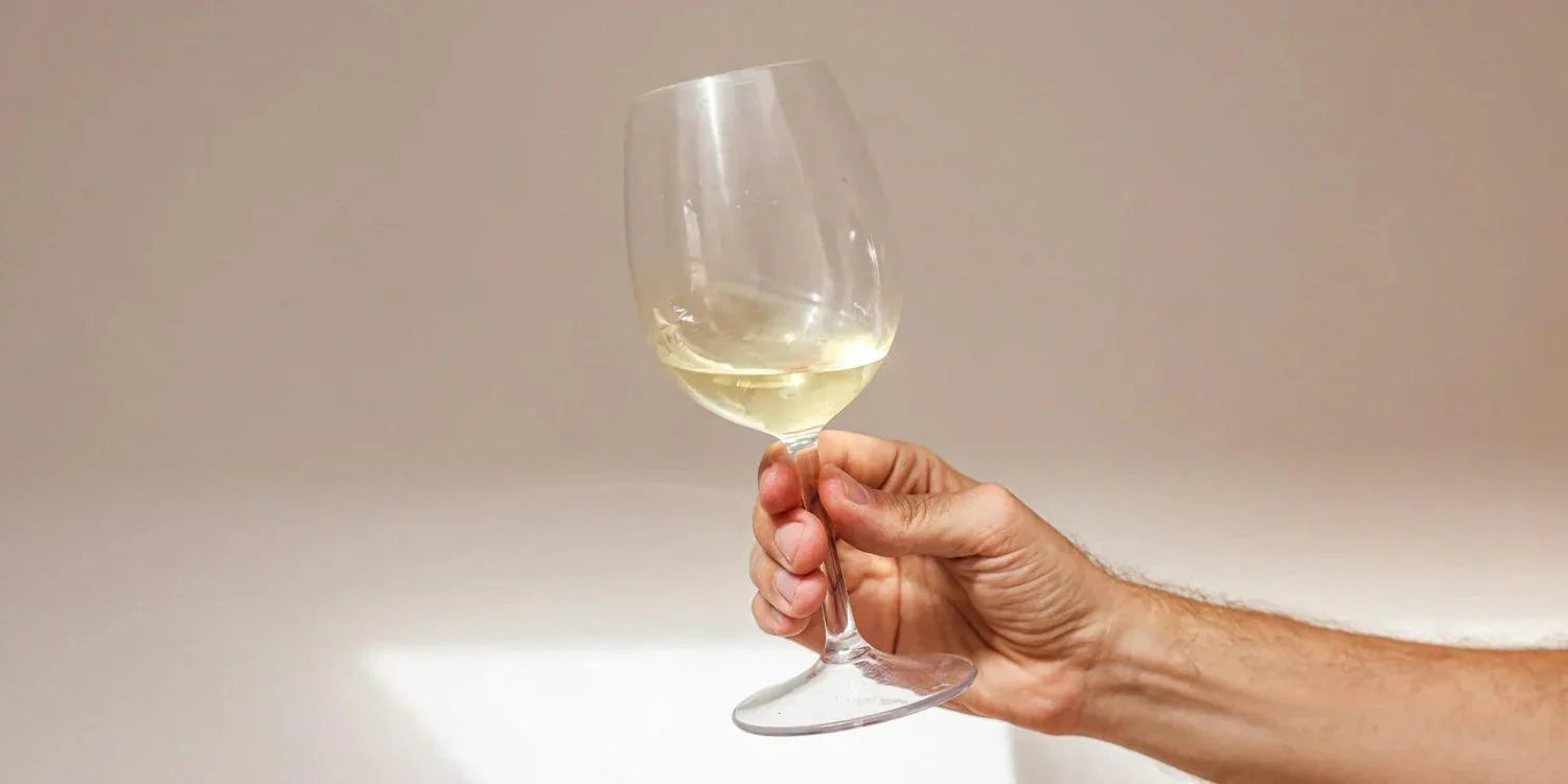 Ein Männerhand hält ein Weinglas gefüllt mit Weißwein